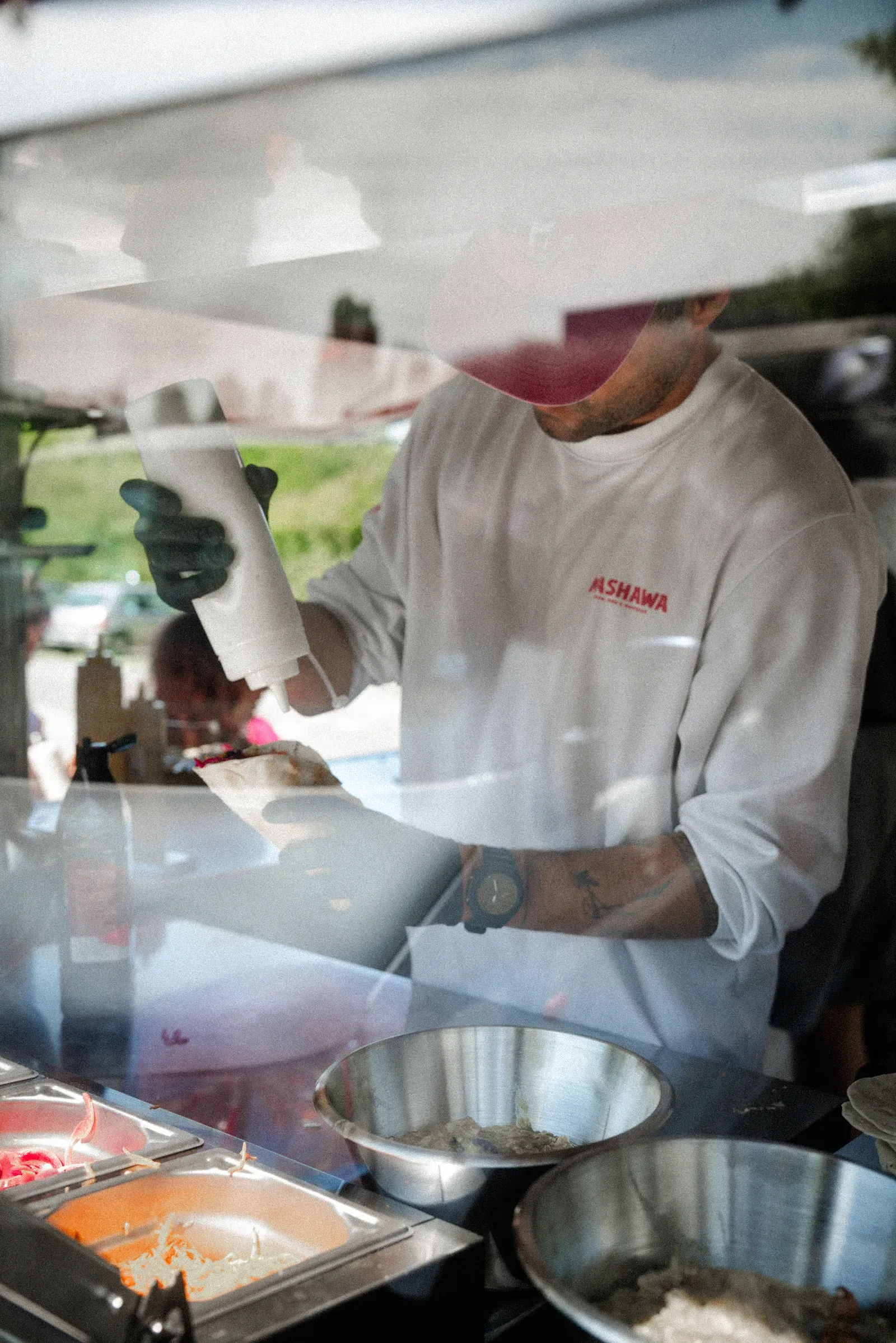 Pierre assaisonnant un shawarma avec une sauce maison, tatouages visibles
